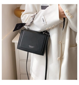 Detail of black crossbody box bag with silk scarf wrapped on the top metal handle