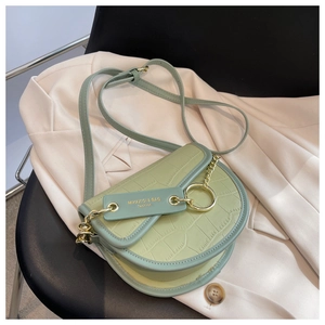 Detailed close-up of light green crocodile embossed saddle bag on beige blazer