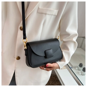 Détail du sac minimaliste en similicuir noir avec boucle dorée sur un costume beige