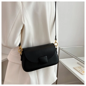 Petit sac carré en cuir noir avec anneaux dorés porté sur une tenue blanche élégante