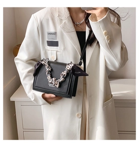 Close-up of a minimalist black square crossbody bag with silk scarf metal chain handle