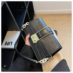 Detail of black crocodile embossed shoulder bag with gold clasp and plastic chain strap