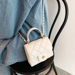 White quilted mini crossbody bag with gold flower clasp and chain strap on a chair