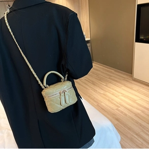 Close-up of sage green quilted mini bag with gold chain strap on a black blazer