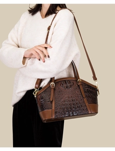 Detail of dark brown crocodile pattern handbag worn by a model in casual attire