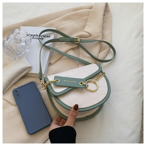 Detail of cream saddle bag with green trim, crocodile texture, and gold hardware