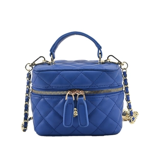 Blue quilted mini box crossbody bag with gold chain strap and top handle on white background