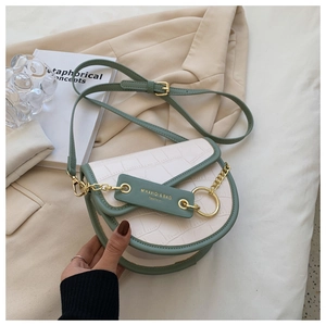 Close-up of cream saddle bag with green crocodile texture trim and gold chain detail