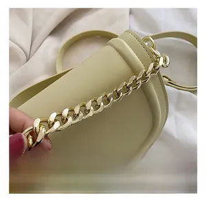 Close-up of beige leather saddle bag featuring a chunky gold metal chain detail