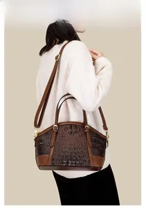 Brown crocodile embossed leather shell bag worn as a shoulder bag on a white coat