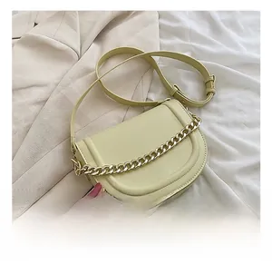 Detailed macro view of light yellow saddle bag featuring a bold gold chain and leather texture