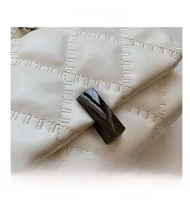 Detailed macro view of the dark glossy metal buckle and quilted stitching on the cream bag