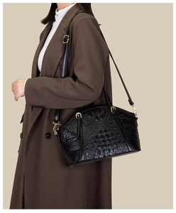 Detail of black crocodile pattern handbag with gold hardware styled on a model in a suit