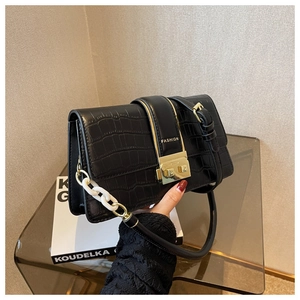 Detail of black crocodile texture handbag with golden buckle and white acrylic chain strap