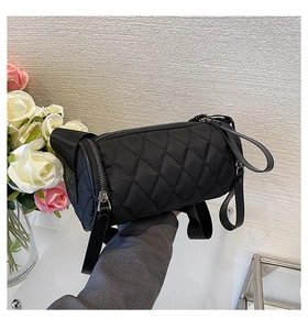 Close-up of black quilted nylon cylinder bag with metal zipper held in a stylish setting