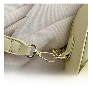 Close-up of golden metal hook buckle and fine stitching on beige leather saddle bag