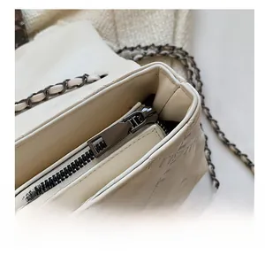 Macro detail of high-quality dark gunmetal zipper and leather chain strap on a cream bag