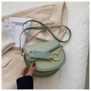 Detail of mint green crocodile pattern saddle bag with gold ring buckle on beige blazer