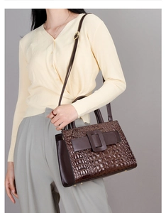 Detail of dark brown crocodile pattern handbag with large square buckle and long strap