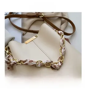 Close-up of cream bucket bag featuring silk scarf wrapped chain handle and gold trim