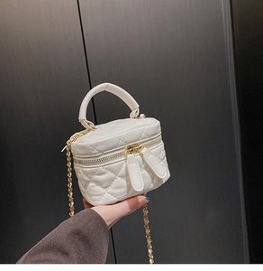Macro detail of a white quilted mini crossbody bag with a gold zipper and chain strap