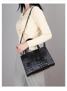 Detail of black crocodile texture handbag with gold metal feet and adjustable shoulder strap