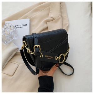 Detail of black crocodile texture saddle bag with gold chain and leather tag