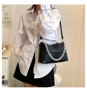 Detail of black matte leather shoulder bag featuring a chunky white acrylic chain strap