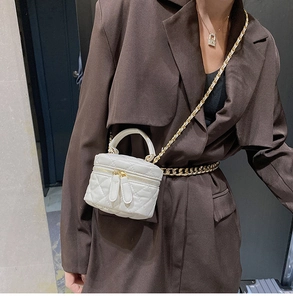 Quilted white mini vanity bag with chain strap and double zipper detail on brown blazer