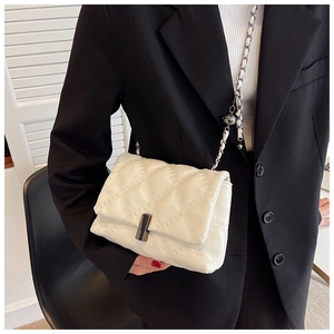 Detail of cream quilted crossbody bag featuring dark grey metal lock and chain strap
