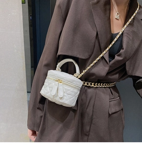 Detail view of a white quilted leather vanity bag with gold chain strap and top handle