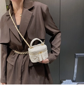 Close-up of a white quilted mini crossbody bag with gold chain strap and dual zipper detail