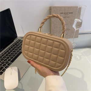 Beige quilted box bag with a twisted handle and gold chain strap in a lifestyle setting