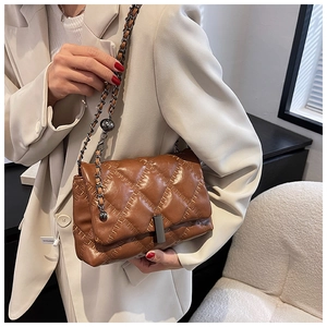 Close-up of brown quilted chain bag featuring a rectangular metal clasp and leather strap
