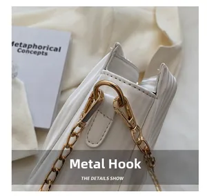 Close-up of golden metal hook and pearl chain on a white pleated crossbody bag