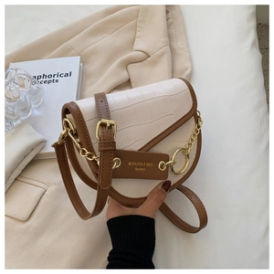 Detail of cream crocodile embossed saddle bag with brown trim and gold chain accents