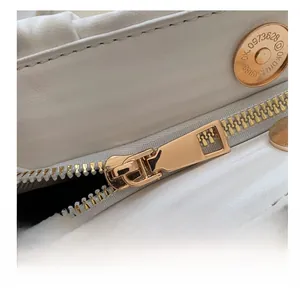 Macro shot of gold metal zipper and numbered magnetic buckle on white leather bag