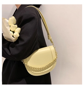 Detail shot of a creamy yellow saddle bag with gold chain and leather strap on a model