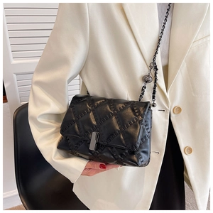 Detail of black quilted chain bag with silver lock and a decorative ball pendant