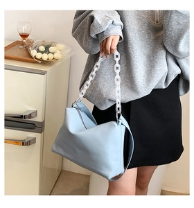 Detail of light blue hobo bag featuring a bold white acrylic chain and matte leather texture
