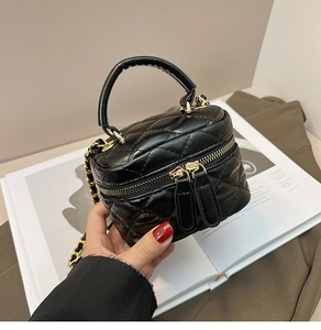 Detail of a quilted black leather mini vanity bag with gold chain and dual zipper closure
