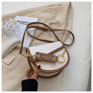 Macro detail of white crocodile pattern saddle bag with brown trim and gold hardware