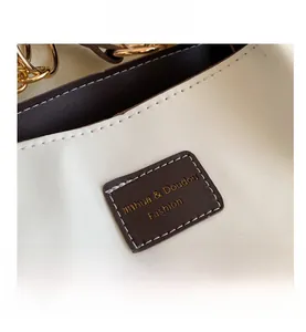 Close-up of white lychee leather texture with brown brand patch and golden chain detail