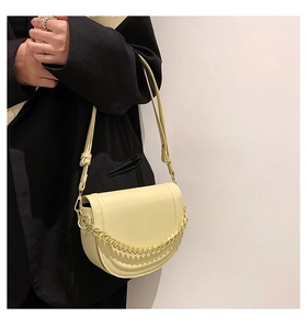 Detail of light yellow saddle bag with gold chain and strap worn on a black blazer