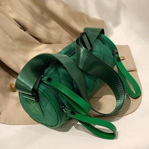 Green quilted nylon cylinder crossbody bag with wide shoulder strap on beige coat background