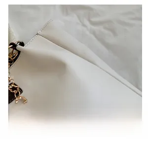 Detail of white tote bag with soft fabric texture and decorative gold flower chain