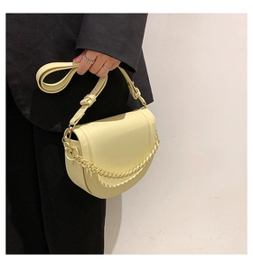 Detail of a creamy yellow saddle bag with a chunky gold chain and knotted leather strap