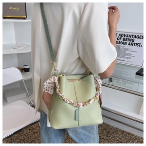 Detail of light green bucket bag with silk scarf handle and metal plate on minimalist background