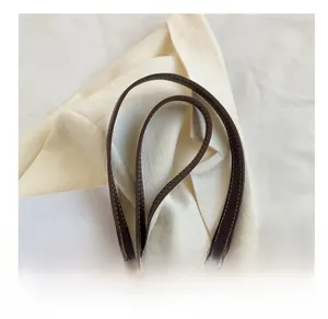 Detail of caramel leather shoulder strap with white contrast stitching and gold buckle