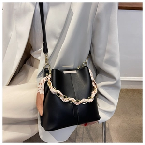 Detail of black leather bucket bag featuring gold chain and floral scarf decoration